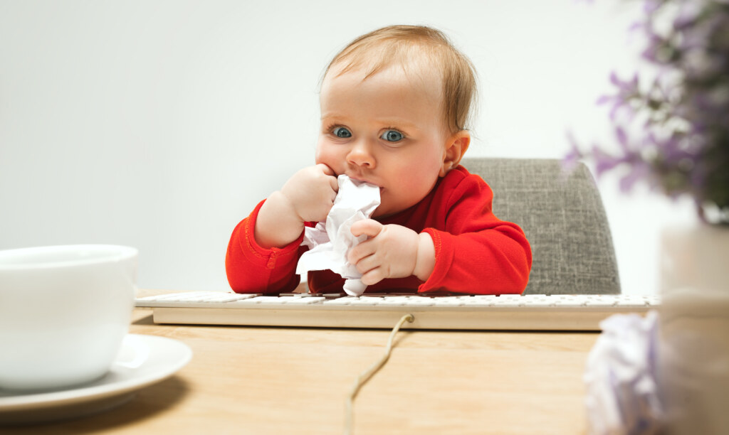Uma bebê sentada com um paninho na boca enquanto está sentado de frente a um teclado 