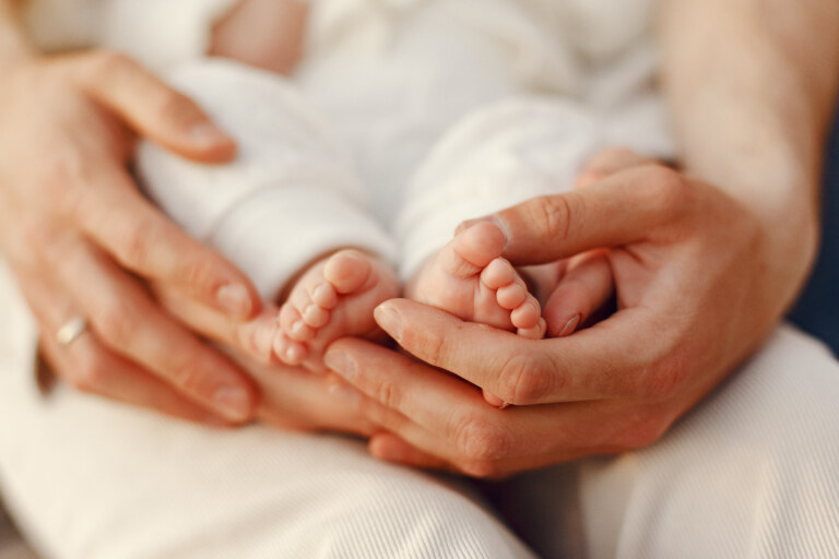 Mãos de uma mulher adulta segurando os pés de um bebê recém nascido