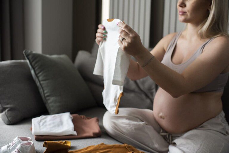 Uma mulher grávida segurando uma roupinha de bebê