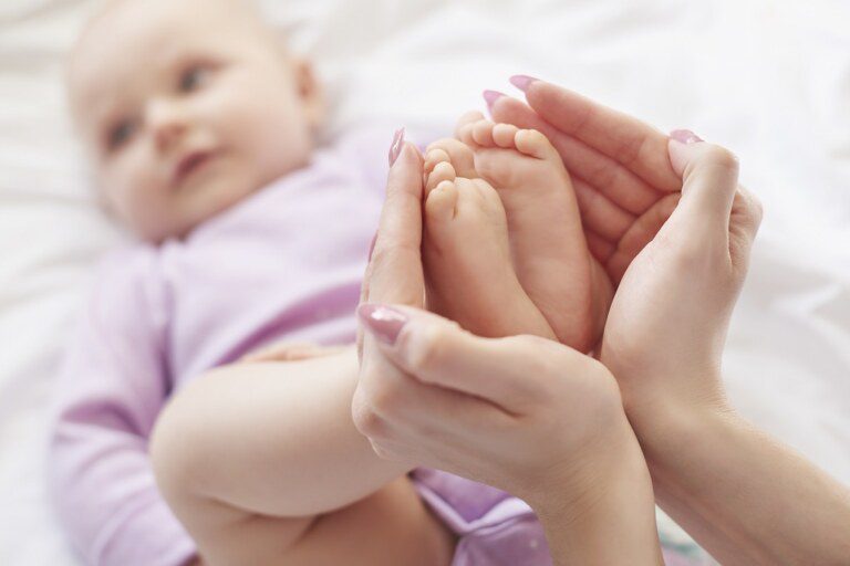 A hand is holding the baby's feet while the baby is lying in the bed