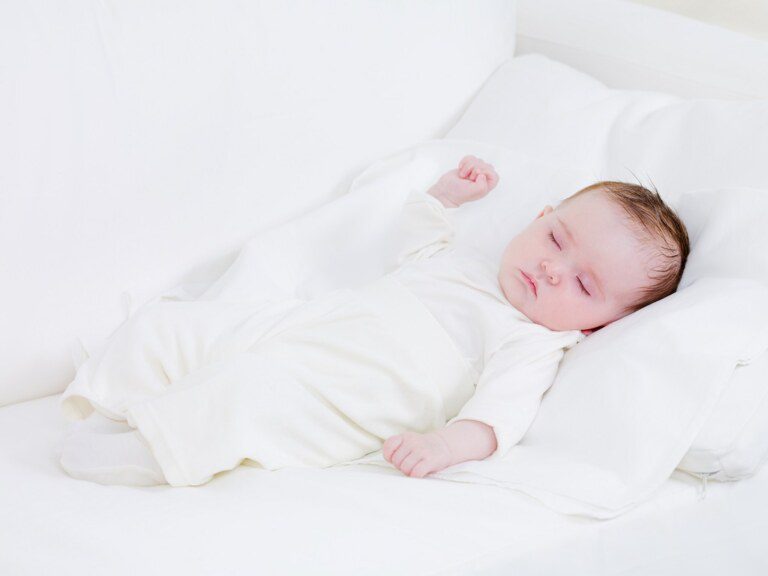 Um bebê vestido com roupas brancas deitado