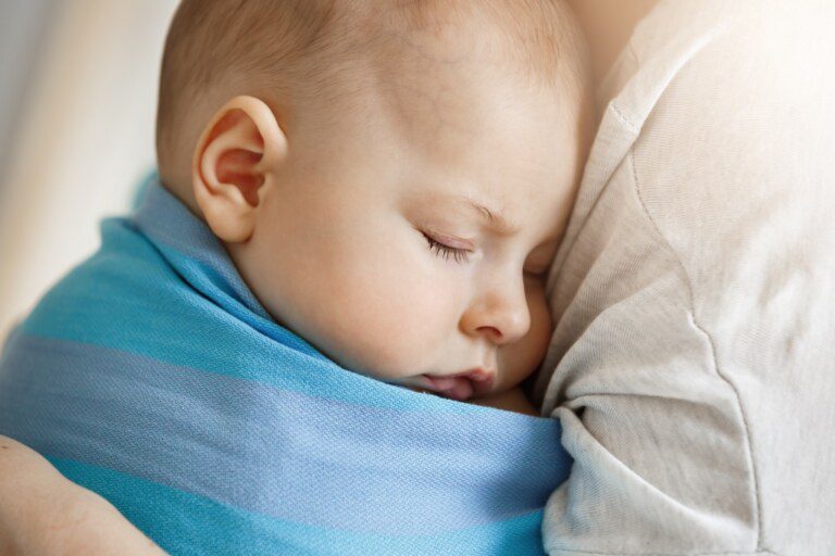 Um bebê dorme embrulhado em uma manta dorme no peito de uma pessoa