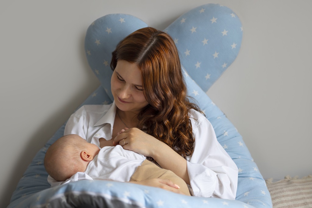 Uma mulher em posição de amamentação com o bebê no colo